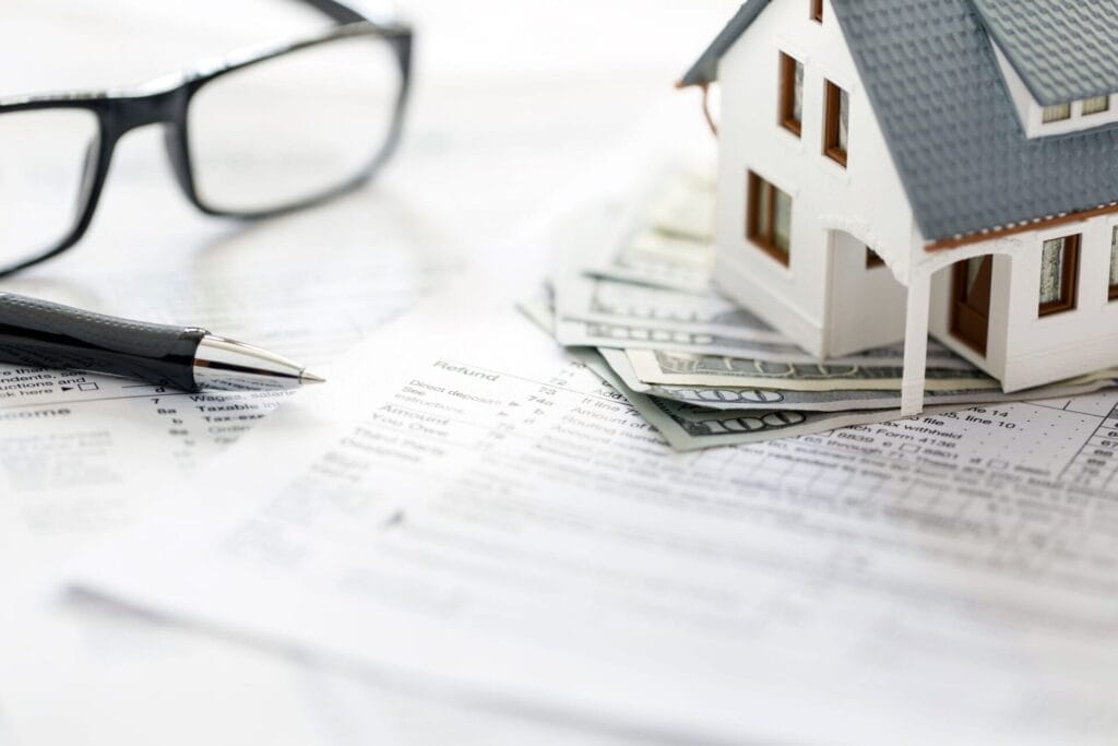 Miniature house with money on tax papers